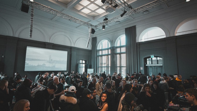 A crowded hall at an all-hands, with a presentation on a large screen behind the room.