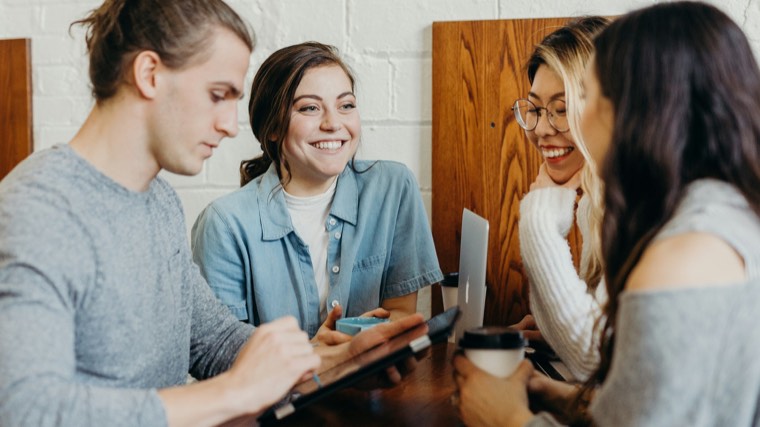 Four colleagues around a cafe table, talking with a tablet and phones in front of them.