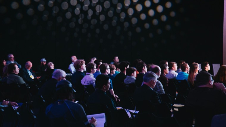 Rows of people seated in a darkened training session, watching something off camera.